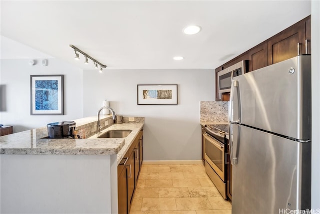 kitchen featuring appliances with stainless steel finishes, kitchen peninsula, sink, and light stone counters