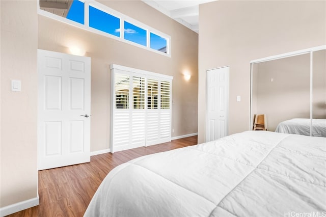 bedroom with hardwood / wood-style flooring, beamed ceiling, and a high ceiling