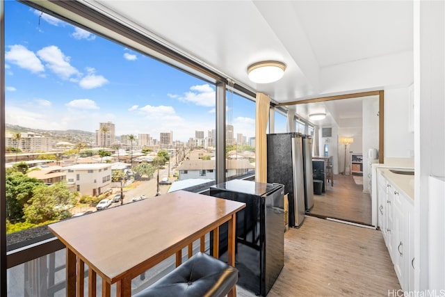 kitchen featuring white cabinets, light wood-type flooring, a wall of windows, and stainless steel fridge