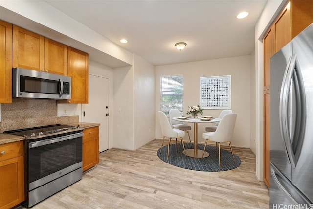 kitchen featuring backsplash, light stone countertops, stainless steel appliances, and light wood-type flooring