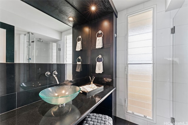 bathroom with vanity, tile walls, a tile shower, and backsplash