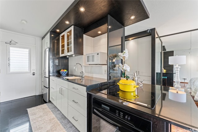 kitchen with black appliances, sink, a barn door, white cabinets, and decorative backsplash