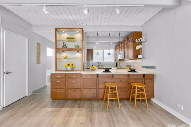 kitchen featuring light hardwood / wood-style flooring, track lighting, sink, beamed ceiling, and a breakfast bar