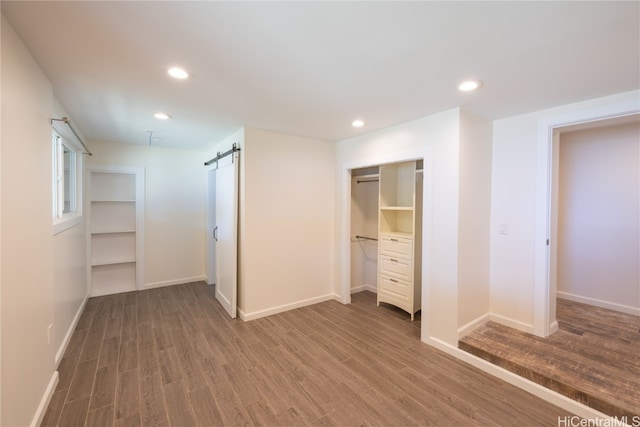 unfurnished bedroom featuring a closet, wood-type flooring, and a barn door