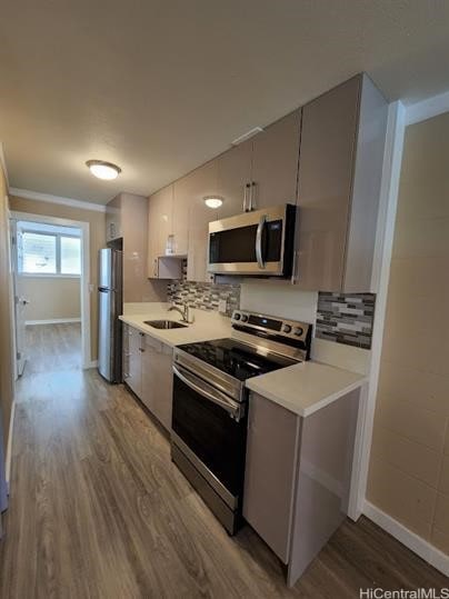 kitchen with decorative backsplash, hardwood / wood-style flooring, ornamental molding, sink, and stainless steel appliances