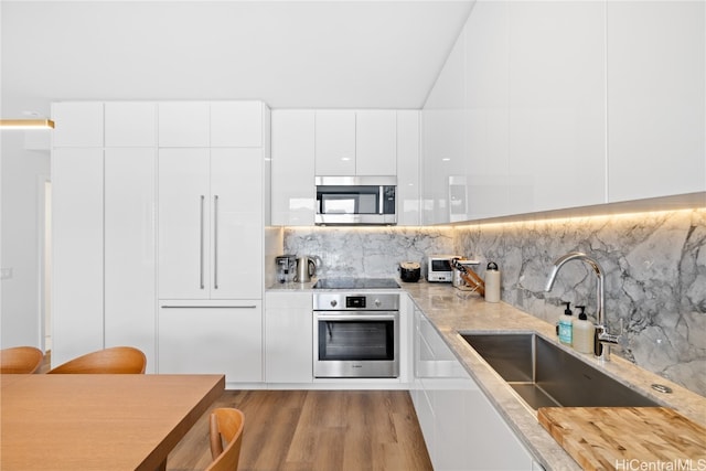 kitchen with sink, decorative backsplash, appliances with stainless steel finishes, light hardwood / wood-style floors, and white cabinetry