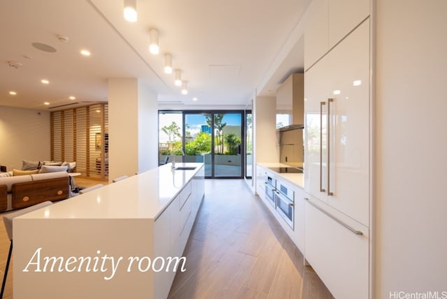 kitchen with floor to ceiling windows, white cabinetry, oven, light hardwood / wood-style floors, and black electric stovetop