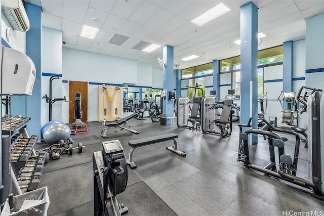 gym featuring an AC wall unit, a drop ceiling, and plenty of natural light