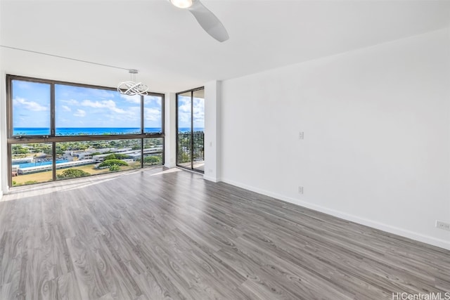 empty room with a wall of windows, wood-type flooring, a water view, and ceiling fan