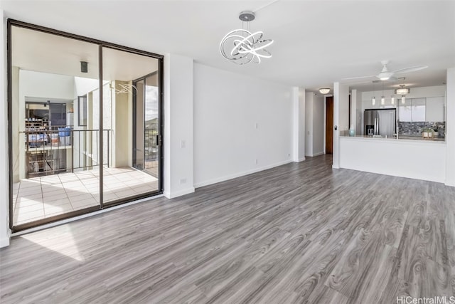 unfurnished living room featuring ceiling fan with notable chandelier and light wood-type flooring