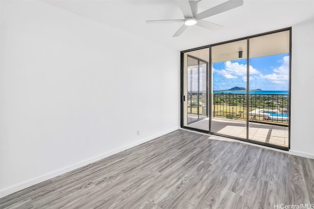 unfurnished room featuring a water view, ceiling fan, light wood-type flooring, and floor to ceiling windows