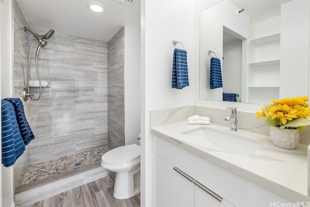 bathroom with vanity, toilet, tiled shower, and hardwood / wood-style floors