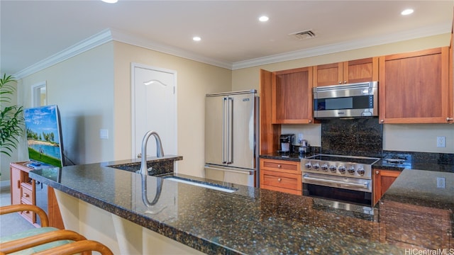 kitchen featuring ornamental molding, dark stone countertops, premium appliances, and a kitchen bar