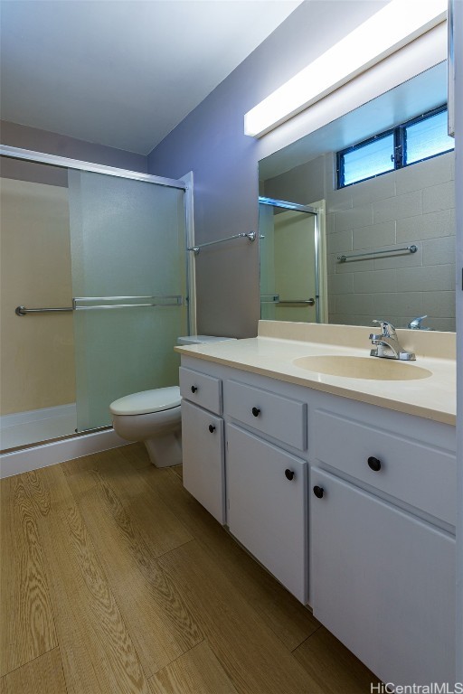 bathroom with vanity, toilet, wood-type flooring, and a shower with shower door