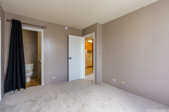 unfurnished bedroom featuring ensuite bath, a textured ceiling, white refrigerator, and light colored carpet