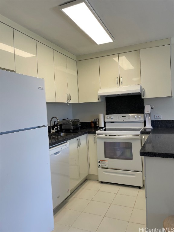 kitchen with white appliances, light tile patterned floors, dark stone countertops, and sink