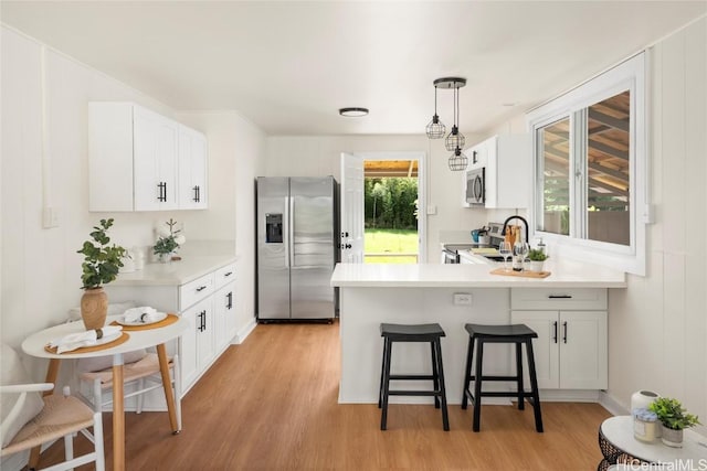 kitchen with a breakfast bar, light wood-style flooring, stainless steel appliances, a peninsula, and light countertops