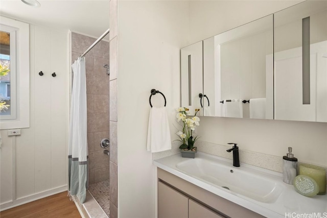 full bath with tiled shower, wood finished floors, and vanity