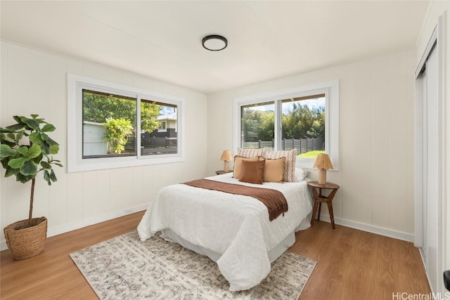 bedroom with multiple windows, wood finished floors, and baseboards