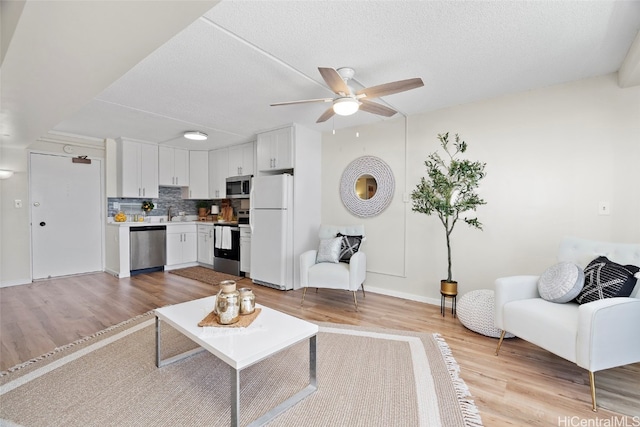 living room featuring a textured ceiling, light wood-type flooring, and ceiling fan