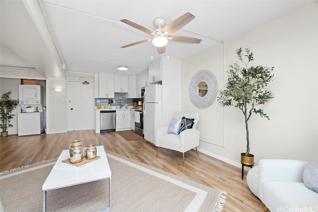 living room featuring stacked washer / dryer, light hardwood / wood-style floors, and ceiling fan