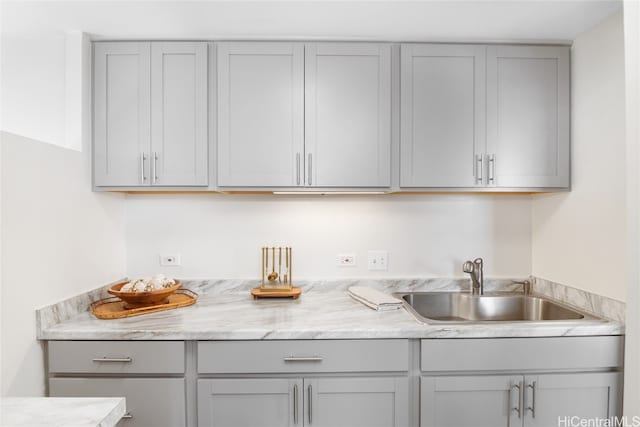 kitchen featuring gray cabinetry, sink, and light stone counters