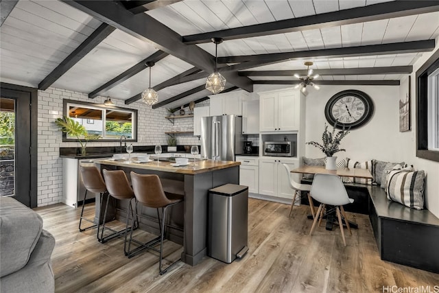 kitchen with appliances with stainless steel finishes, hanging light fixtures, white cabinets, brick wall, and light hardwood / wood-style flooring