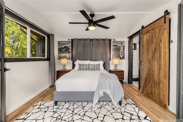 bedroom featuring a barn door, light wood-type flooring, and ceiling fan