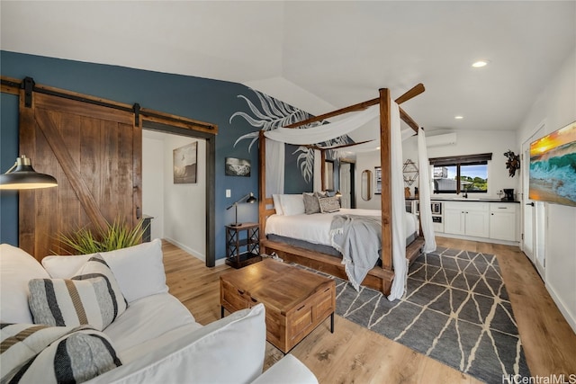 bedroom with lofted ceiling, a barn door, light hardwood / wood-style flooring, and a wall unit AC