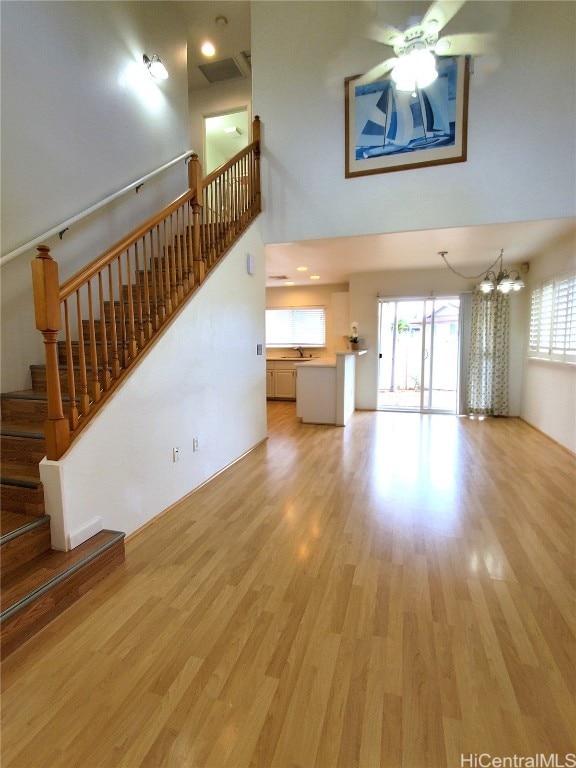 unfurnished living room featuring a towering ceiling, light hardwood / wood-style flooring, and ceiling fan with notable chandelier