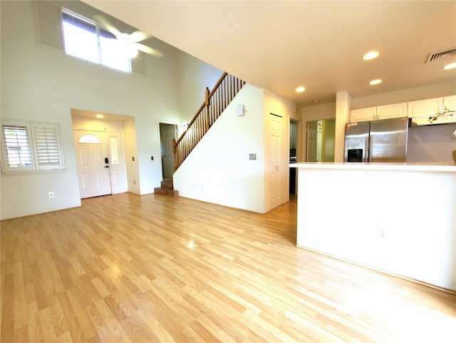 unfurnished living room with light hardwood / wood-style flooring, a towering ceiling, and ceiling fan