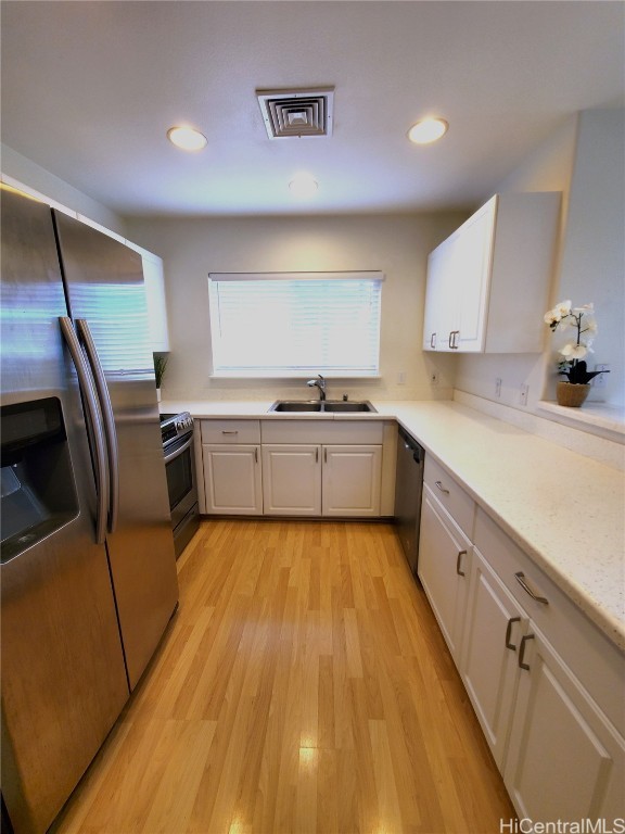 kitchen featuring appliances with stainless steel finishes, white cabinets, sink, and light wood-type flooring