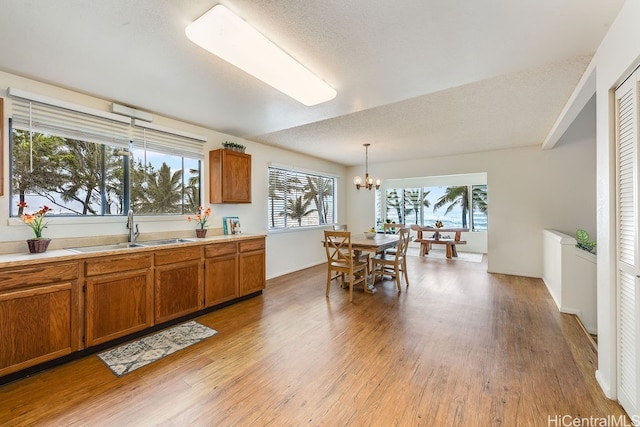 kitchen featuring sink, hanging light fixtures, light wood-type flooring, a textured ceiling, and a notable chandelier