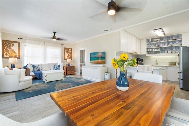dining room featuring crown molding, a ceiling fan, light wood finished floors, and visible vents