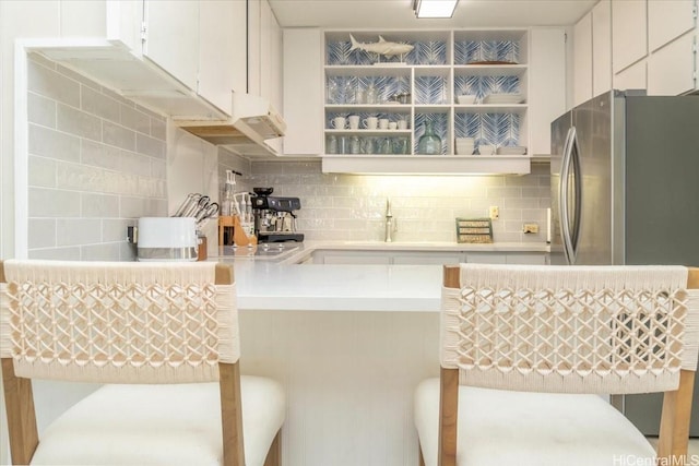kitchen featuring freestanding refrigerator, a peninsula, tasteful backsplash, and light countertops