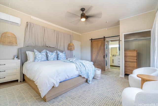 bedroom featuring ceiling fan, a wall mounted AC, a barn door, and ensuite bathroom