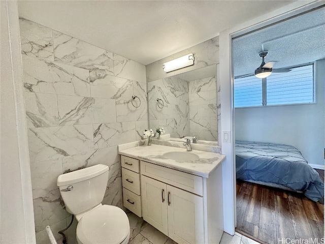 bathroom with wood-type flooring, tile walls, vanity, ceiling fan, and toilet