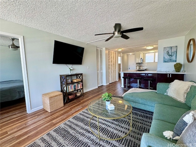 living area with baseboards, a textured ceiling, dark wood-style floors, and a ceiling fan