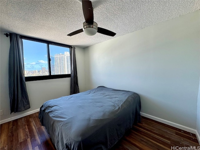 bedroom with ceiling fan, baseboards, wood finished floors, a view of city, and a textured ceiling