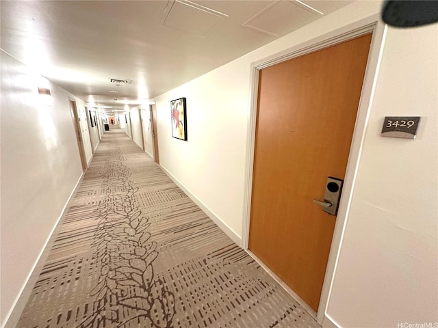 hallway with attic access, visible vents, light carpet, and baseboards
