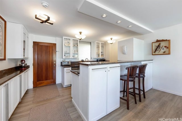 kitchen with kitchen peninsula, white cabinetry, dark stone countertops, and light wood-type flooring