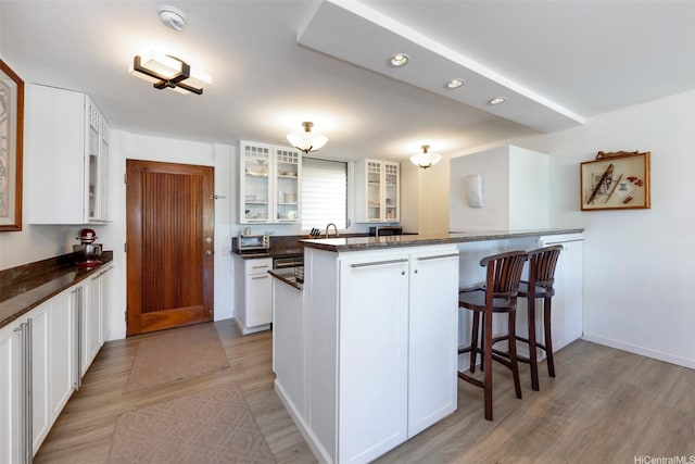 2895 Kalakaua Ave Unit 505, Honolulu, HI 96815 - kitchen featuring light wood-style floors, a kitchen bar, glass insert cabinets, white cabinets, and recessed lighting