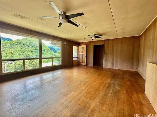 empty room with wooden walls, wood-type flooring, and ceiling fan