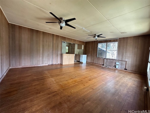 unfurnished living room with hardwood / wood-style floors, ceiling fan, and wood walls