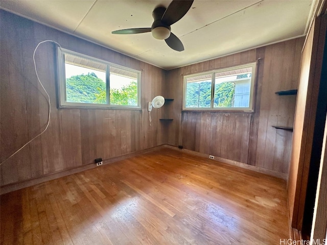 empty room featuring light hardwood / wood-style flooring, ceiling fan, a healthy amount of sunlight, and wood walls