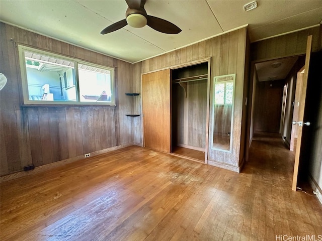 unfurnished bedroom with a closet, wood walls, hardwood / wood-style flooring, and ceiling fan