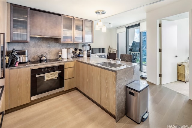 kitchen featuring oven, kitchen peninsula, sink, light hardwood / wood-style floors, and decorative light fixtures