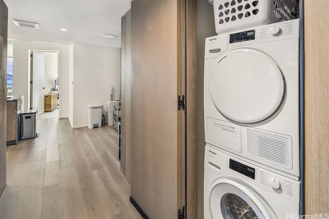 clothes washing area featuring light hardwood / wood-style flooring and stacked washer / dryer