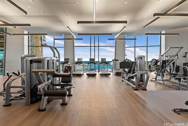 workout area with expansive windows, hardwood / wood-style floors, and a water view