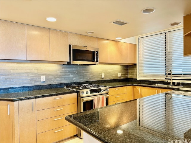 kitchen featuring light brown cabinets, dark stone countertops, sink, appliances with stainless steel finishes, and tasteful backsplash